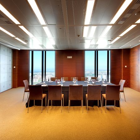 Hotel Eurostars Madrid Tower Esterno foto The photo shows a modern conference room or meeting space. It features a large rectangular table surrounded by several leather chairs. The room has wooden paneling and large windows that let in natural light, providing a view of the outside landscape