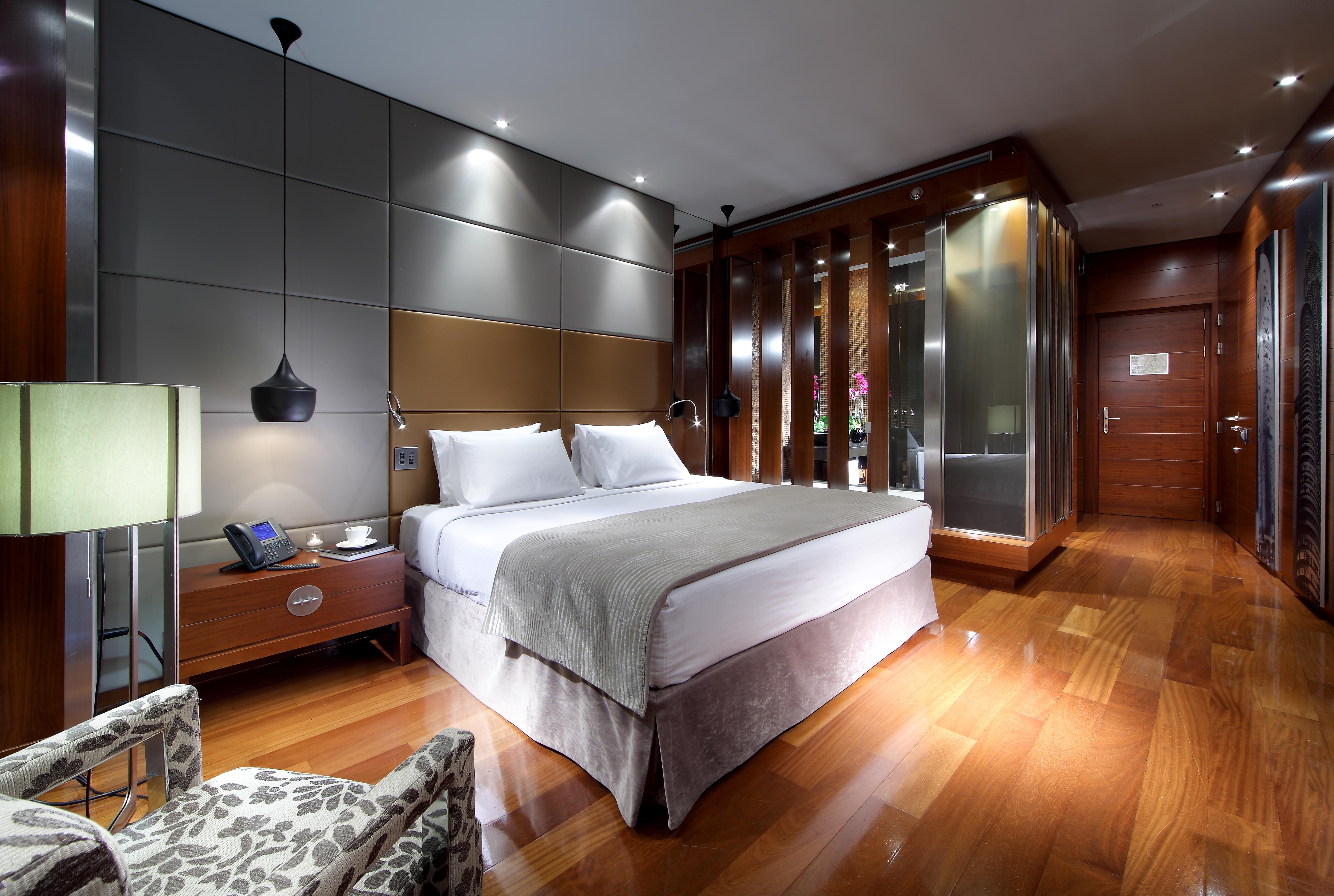 Hotel Eurostars Madrid Tower Esterno foto The photo shows a modern hotel room featuring a double bed dressed in white linens with a light gray blanket. Beside the bed, there is a stylish nightstand with a lamp and a phone. The room has a sleek design with wooden flooring and contemporary dec