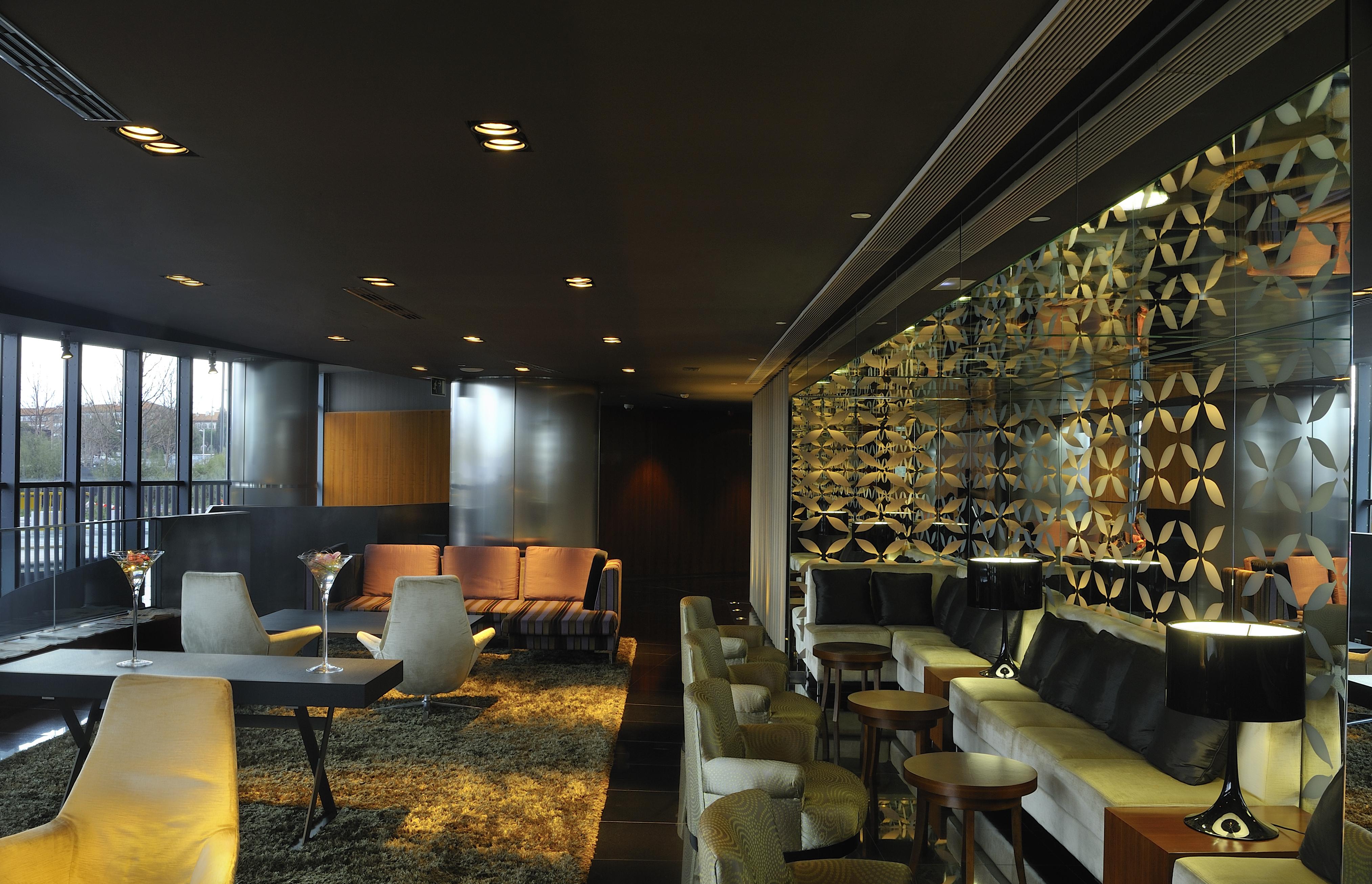 Hotel Eurostars Madrid Tower Esterno foto The photo shows a contemporary and stylish interior space, likely a lounge or bar. The design features a mix of seating arrangements, including plush chairs and modern sofas, set against a dark backdrop with soft lighting. A decorative wall with an i