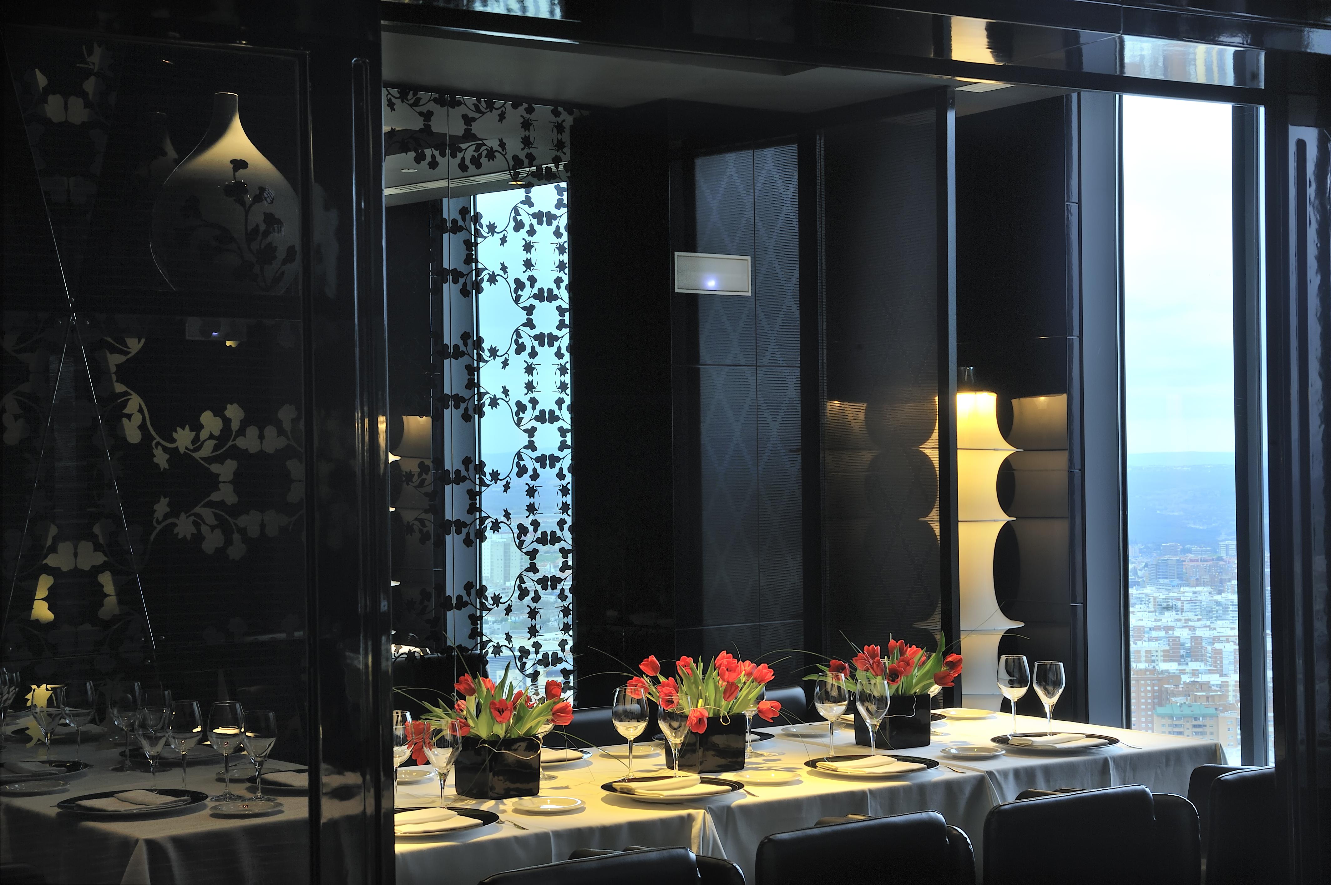 Hotel Eurostars Madrid Tower Esterno foto The photo shows a stylishly decorated dining area with a long table set for a meal. The table is adorned with elegant plates, glasses, and small vases of vibrant tulips as centerpieces. The interior design features a mix of dark and light elements, w