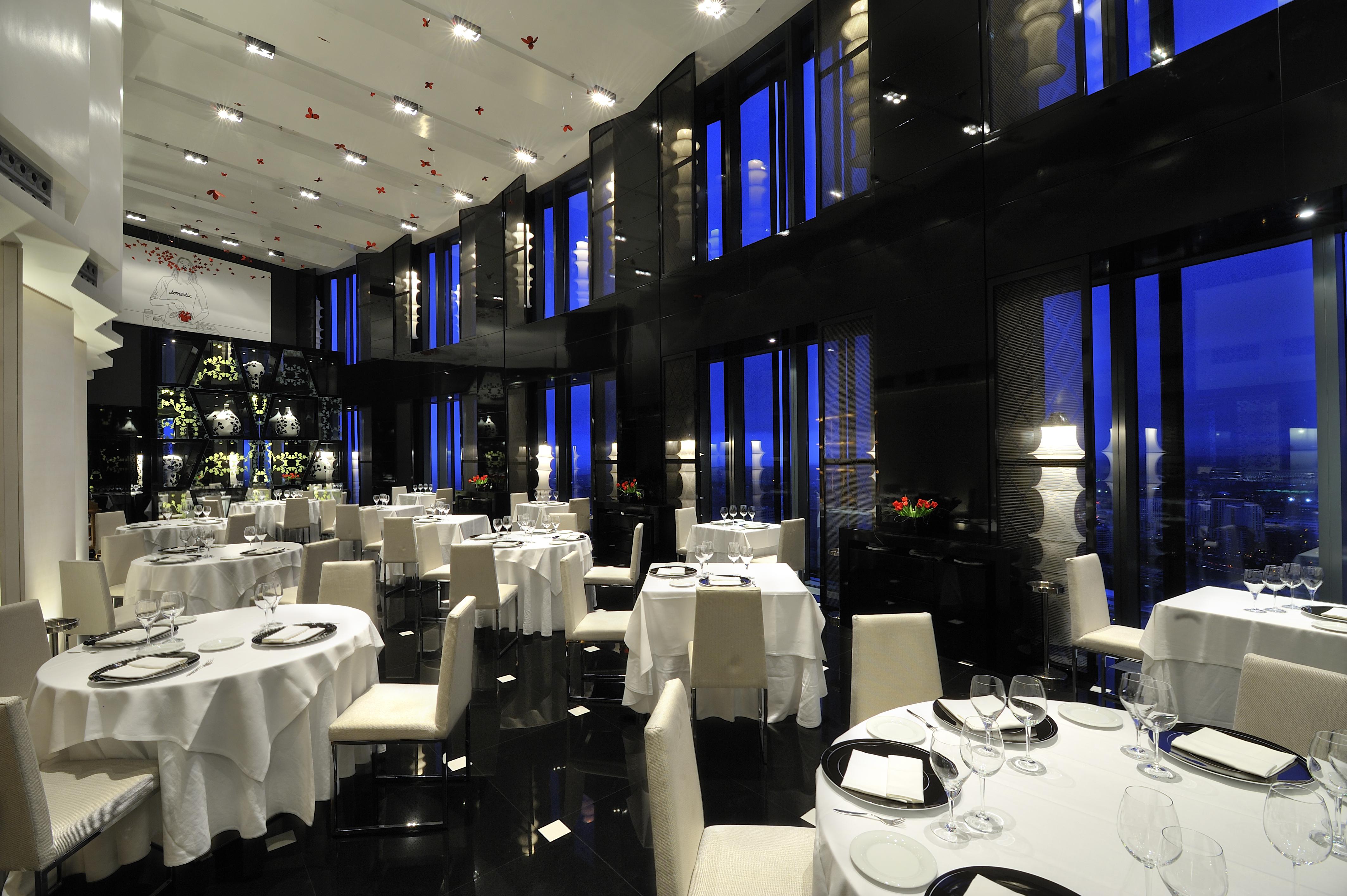 Hotel Eurostars Madrid Tower Esterno foto The photo shows an elegant restaurant interior, characterized by its modern design and luxurious ambiance. The space features several round dining tables, each set with white tablecloths and tableware, including wine glasses. The walls are made of da