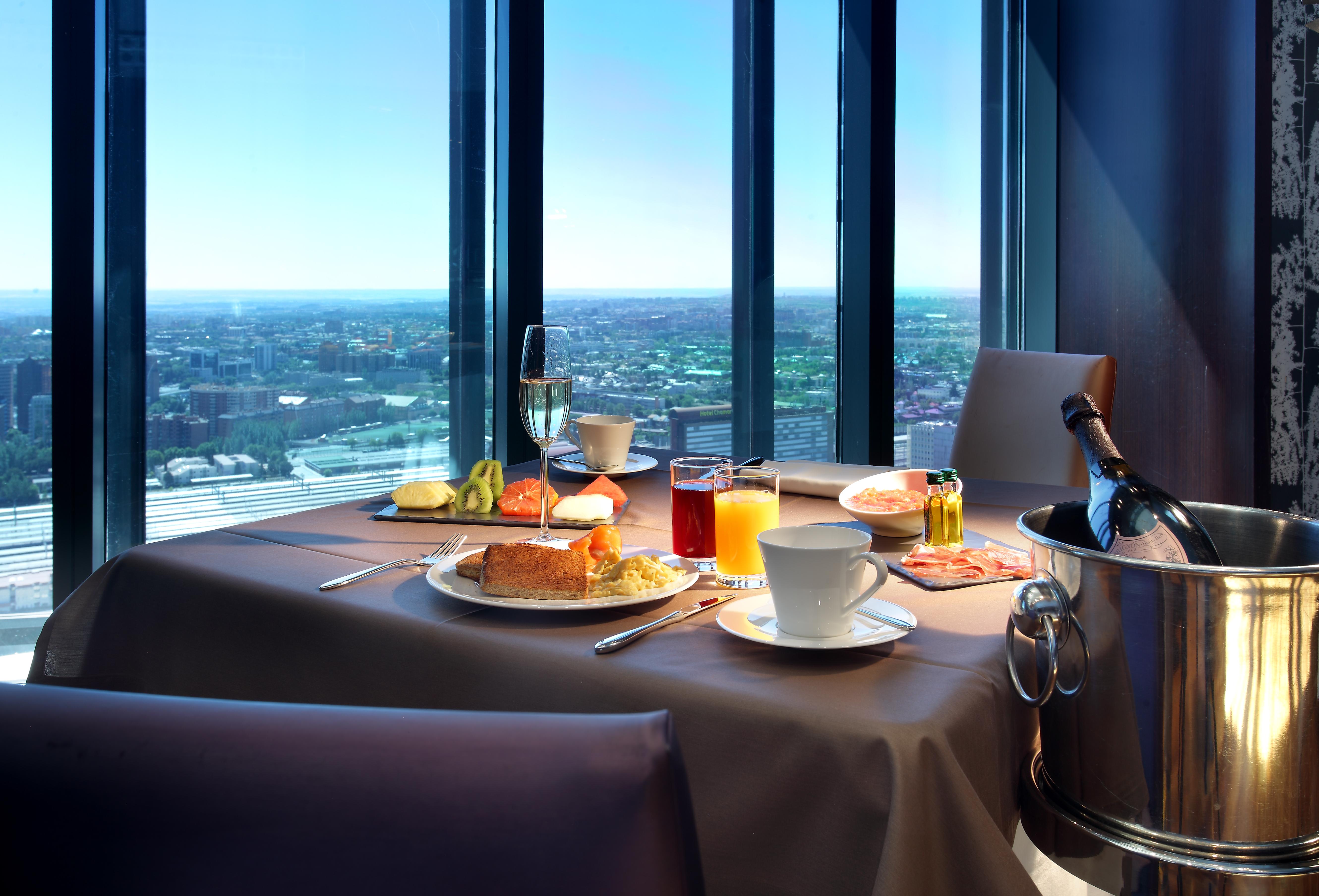 Hotel Eurostars Madrid Tower Esterno foto The photo shows a beautifully set table with a scenic view through large windows. On the table, there are various food items, including a breakfast plate with items like eggs, pastries, and fruit. There are drinks, including a cup of coffee, a glass 