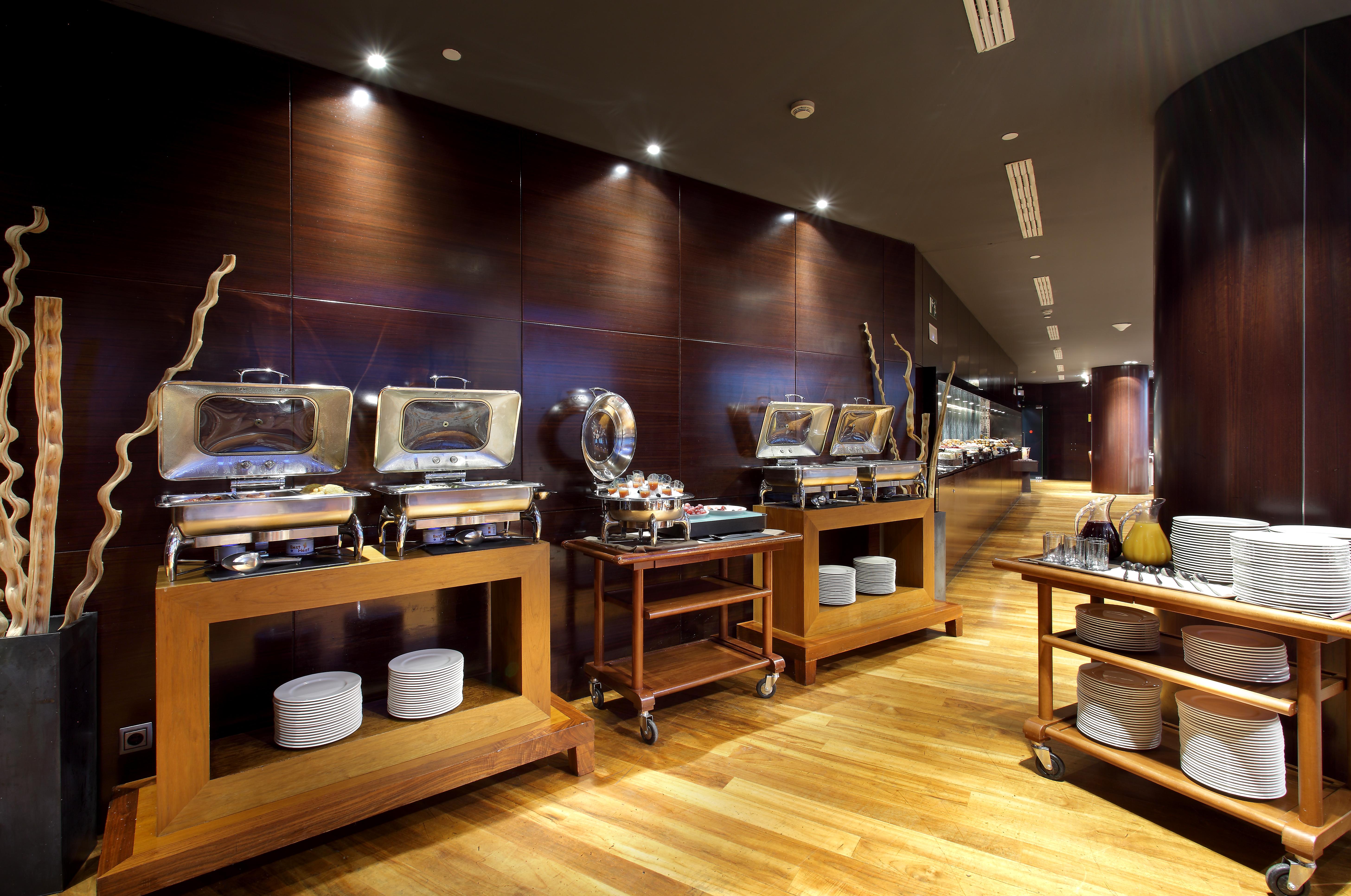 Hotel Eurostars Madrid Tower Esterno foto The photo shows a modern restaurant buffet setting. There are several food warmers placed on wooden tables, showcasing a variety of dishes. The walls have a dark wood finish, and the lighting is soft and ambient, creating an elegant atmosphere. In fr