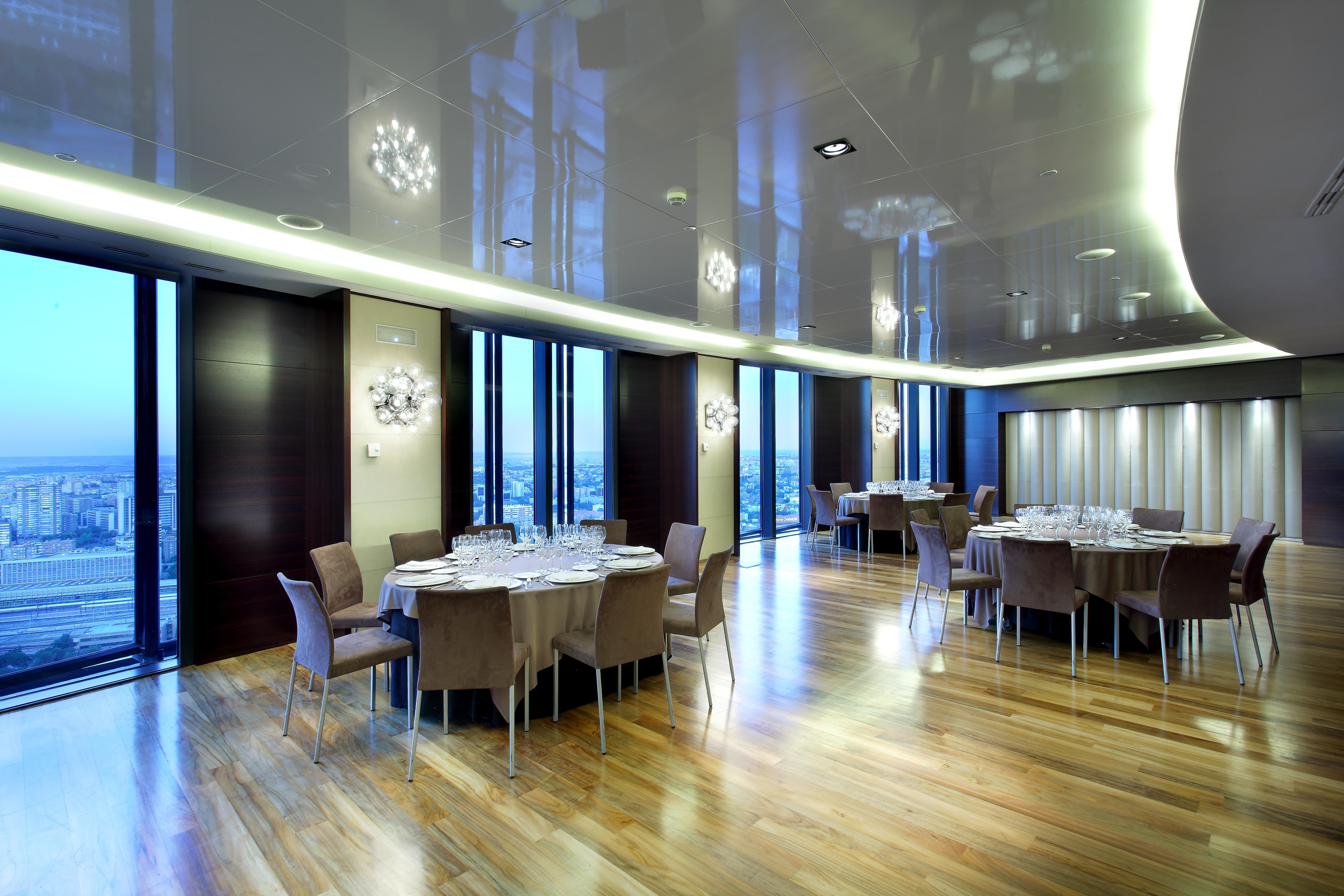 Hotel Eurostars Madrid Tower Esterno foto The photo depicts a modern dining room or banquet hall with large windows that provide a view of the outside. The room features elegant wooden flooring and contemporary furniture, including round tables set with plates, glasses, and cutlery. Various 