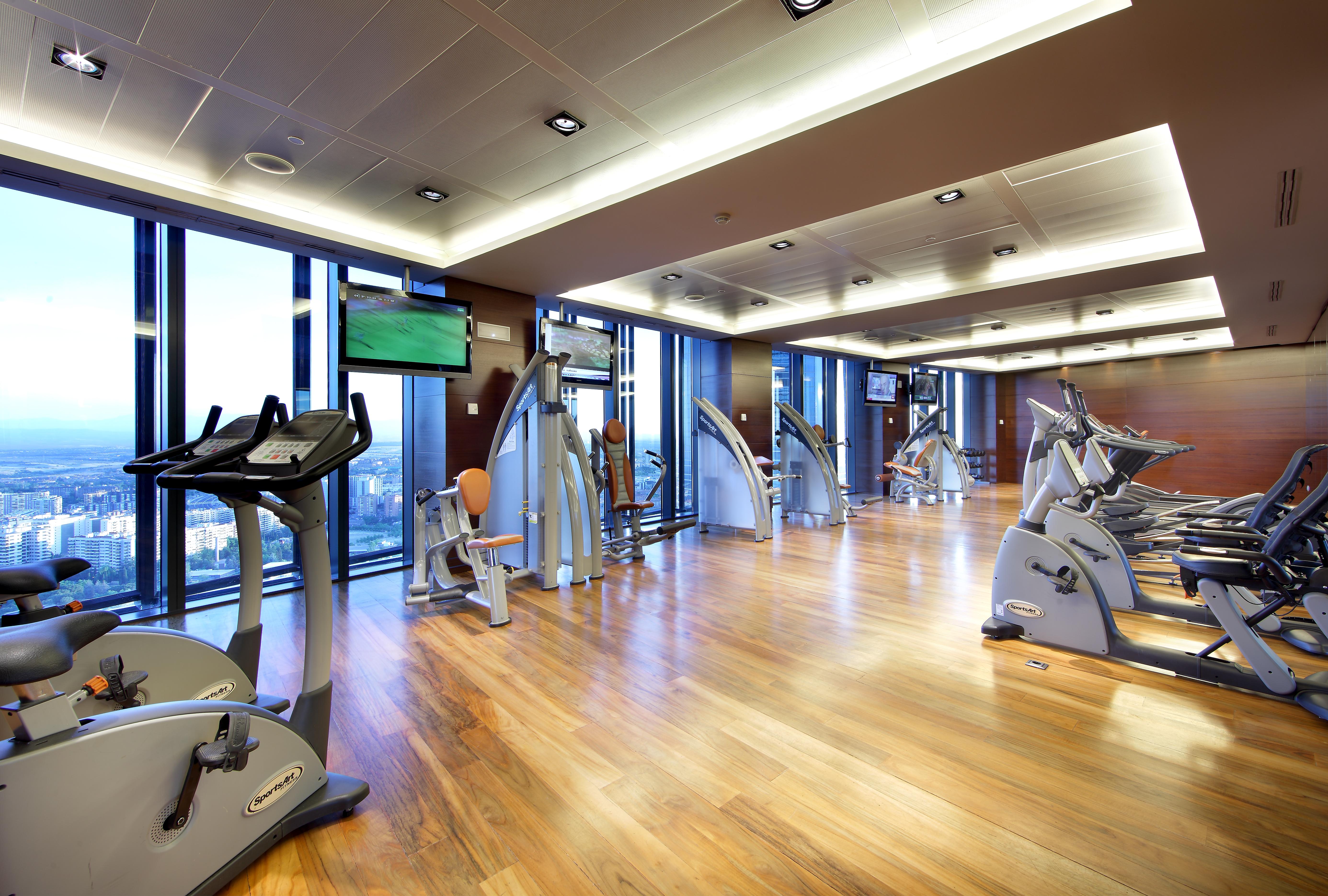 Hotel Eurostars Madrid Tower Esterno foto The photo shows a modern gym or fitness center. It features large windows that let in natural light, providing a view of the outside. The flooring is made of polished wood, giving the space a warm and inviting atmosphere. Various exercise machines ar