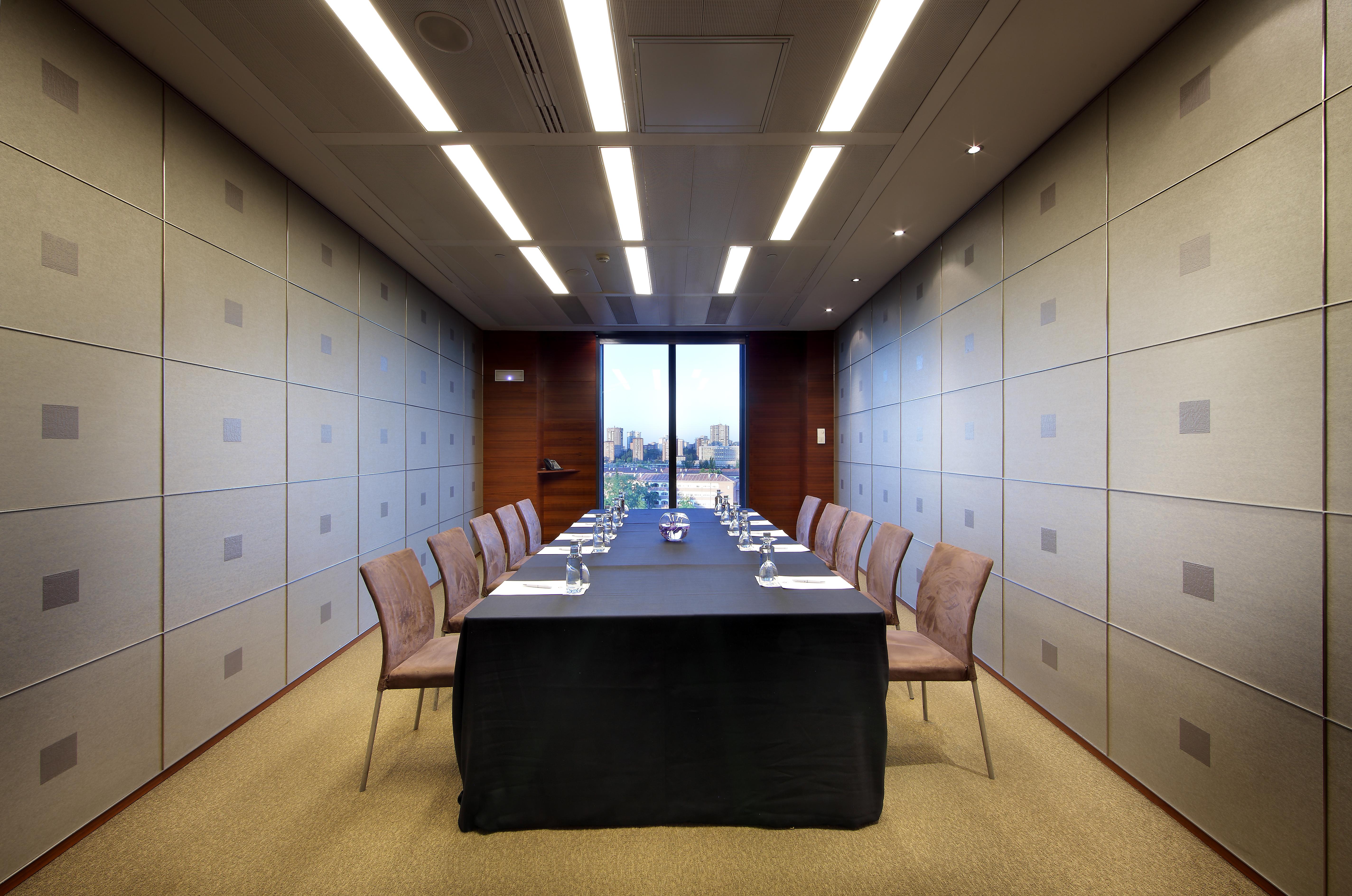 Hotel Eurostars Madrid Tower Esterno foto The photo shows a modern conference room. In the center, there is a long table covered with a black tablecloth. Surrounding the table are several chairs arranged neatly. The walls have a sleek design with light-colored panels, and overhead, there are