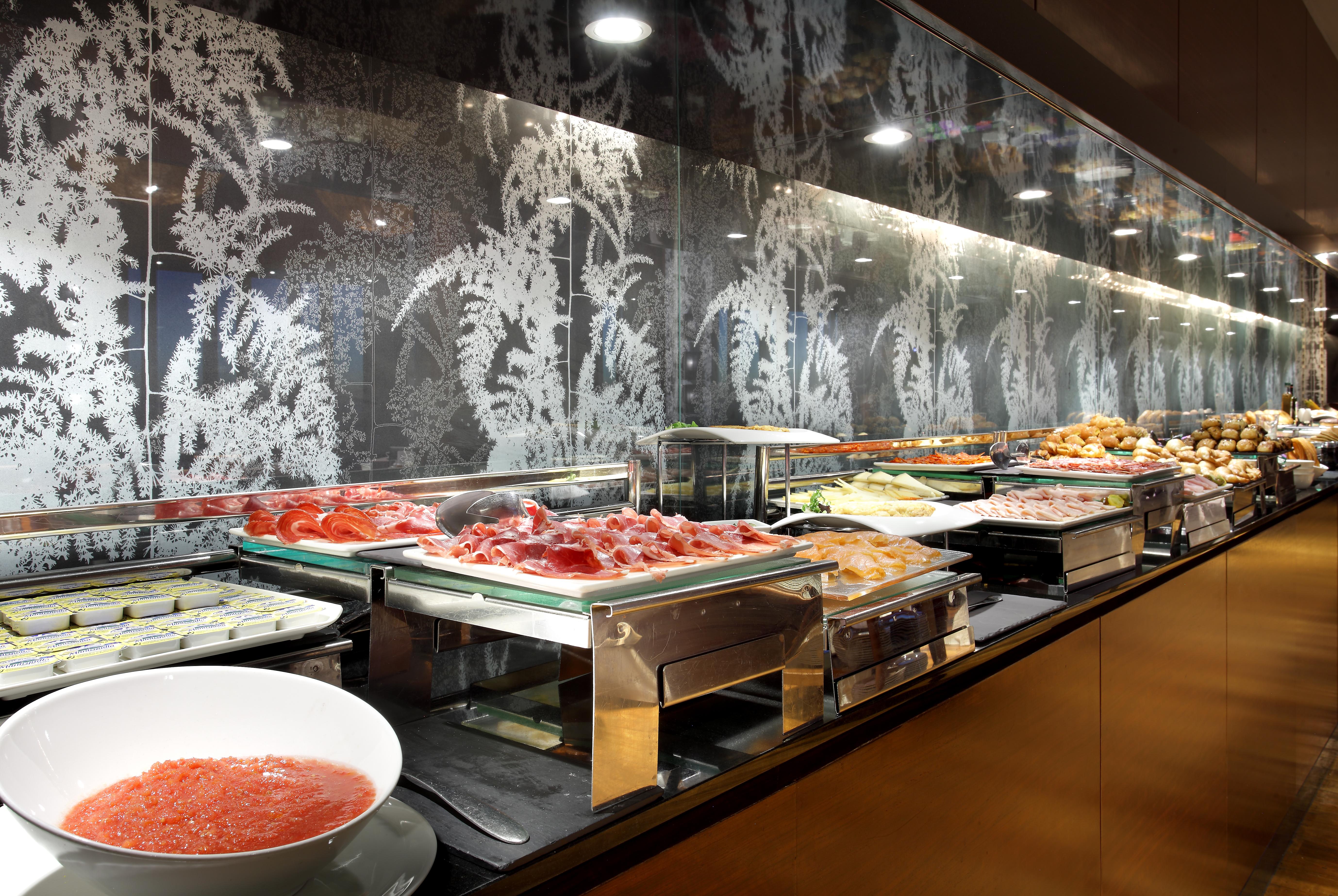 Hotel Eurostars Madrid Tower Esterno foto The photo shows a buffet setup featuring a variety of food items. There are multiple trays and containers displaying an assortment of dishes, including salads, meats, and other prepared foods. A large bowl of sauce or dressing is also visible in fron