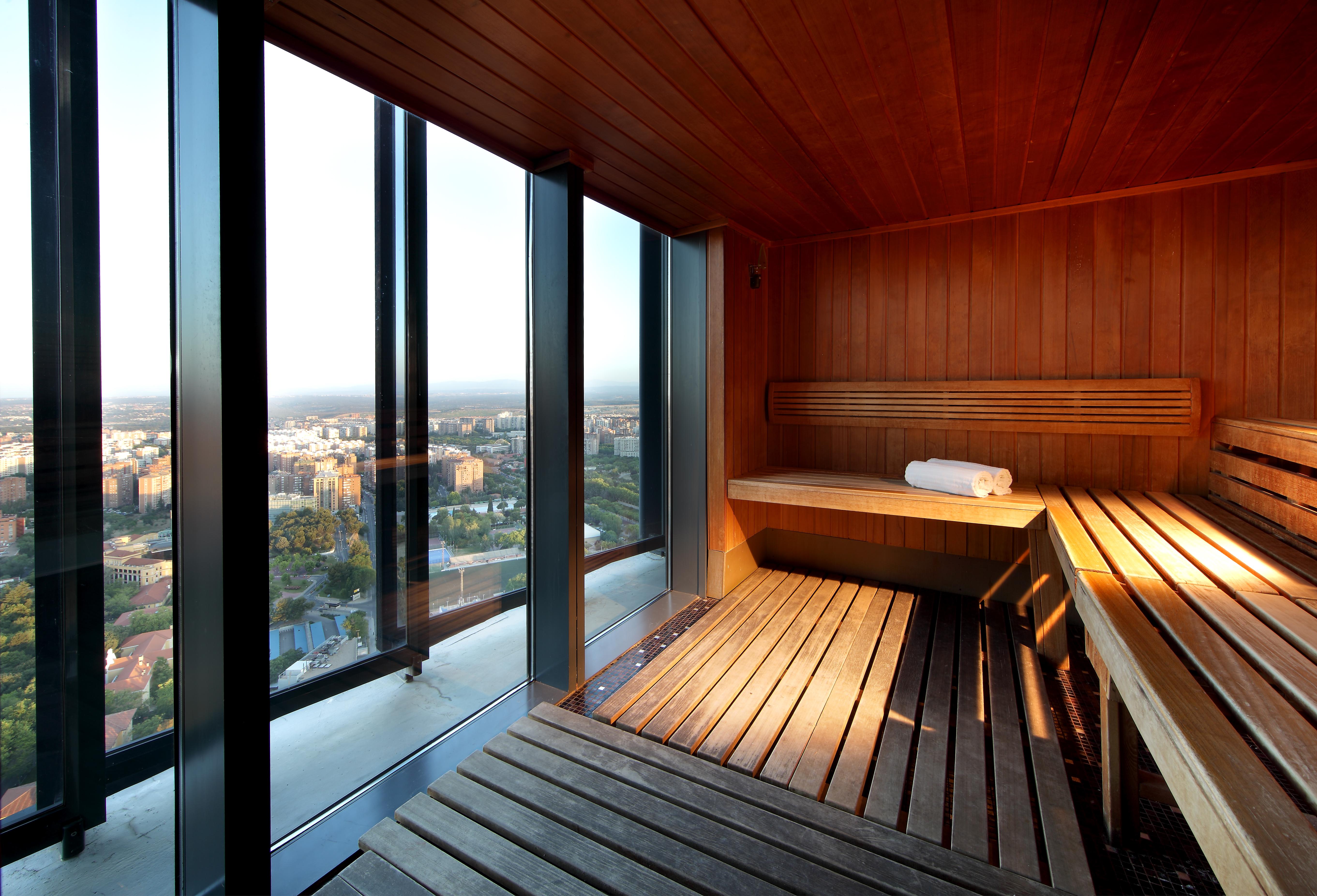 Hotel Eurostars Madrid Tower Esterno foto The image shows a modern sauna with wooden interiors. The sauna features benches made of wood, providing a relaxing space. One of the benches has a rolled towel resting on it. Large glass windows allow for a panoramic view of the outside, showcasing 