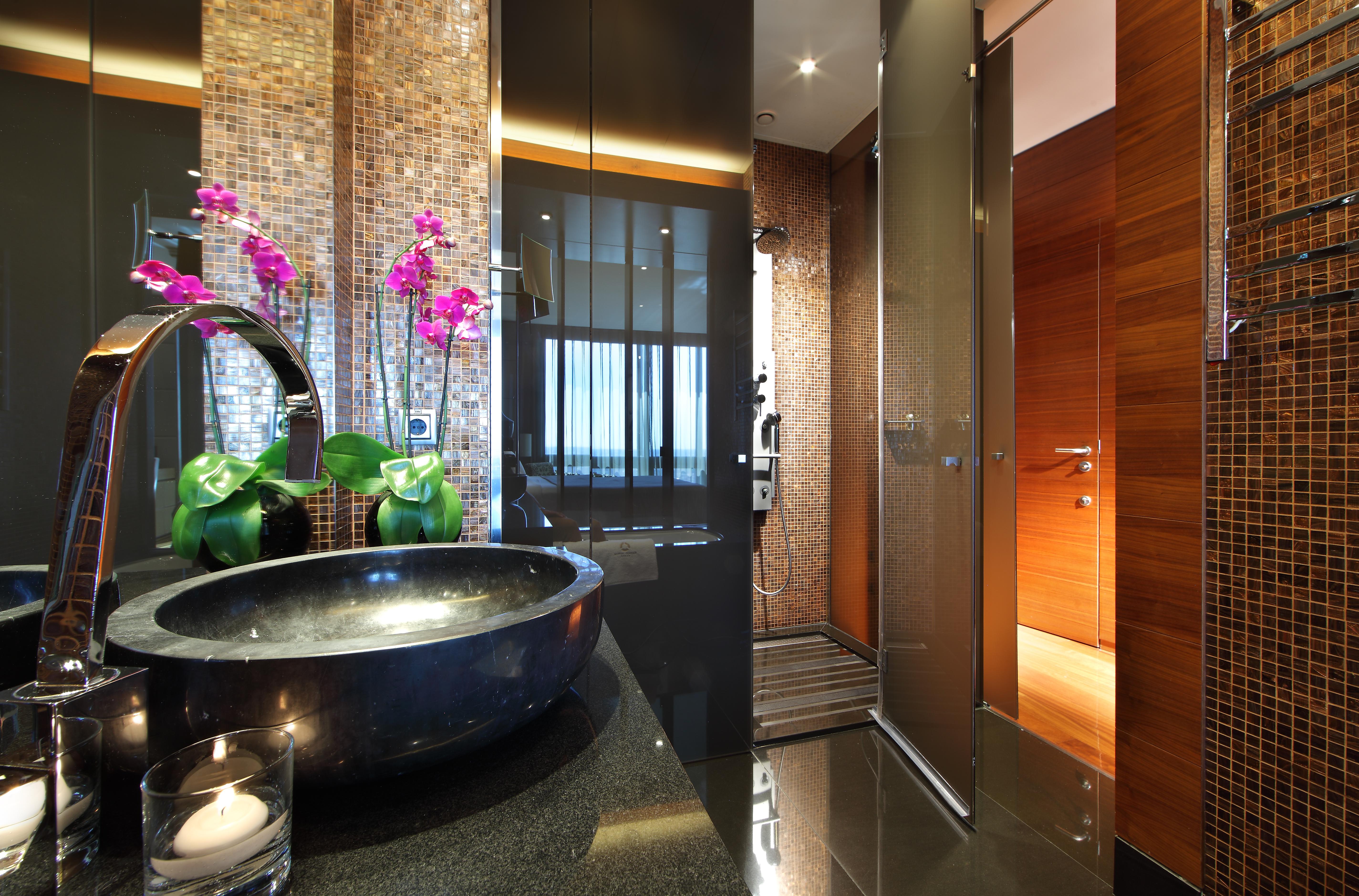 Hotel Eurostars Madrid Tower Esterno foto The photo shows a modern and stylish bathroom. On the left, there is a sleek black basin set on a dark countertop, adorned with decorative elements such as a candle and potted green plants. To the side, there are elegant pink orchids adding a pop of 