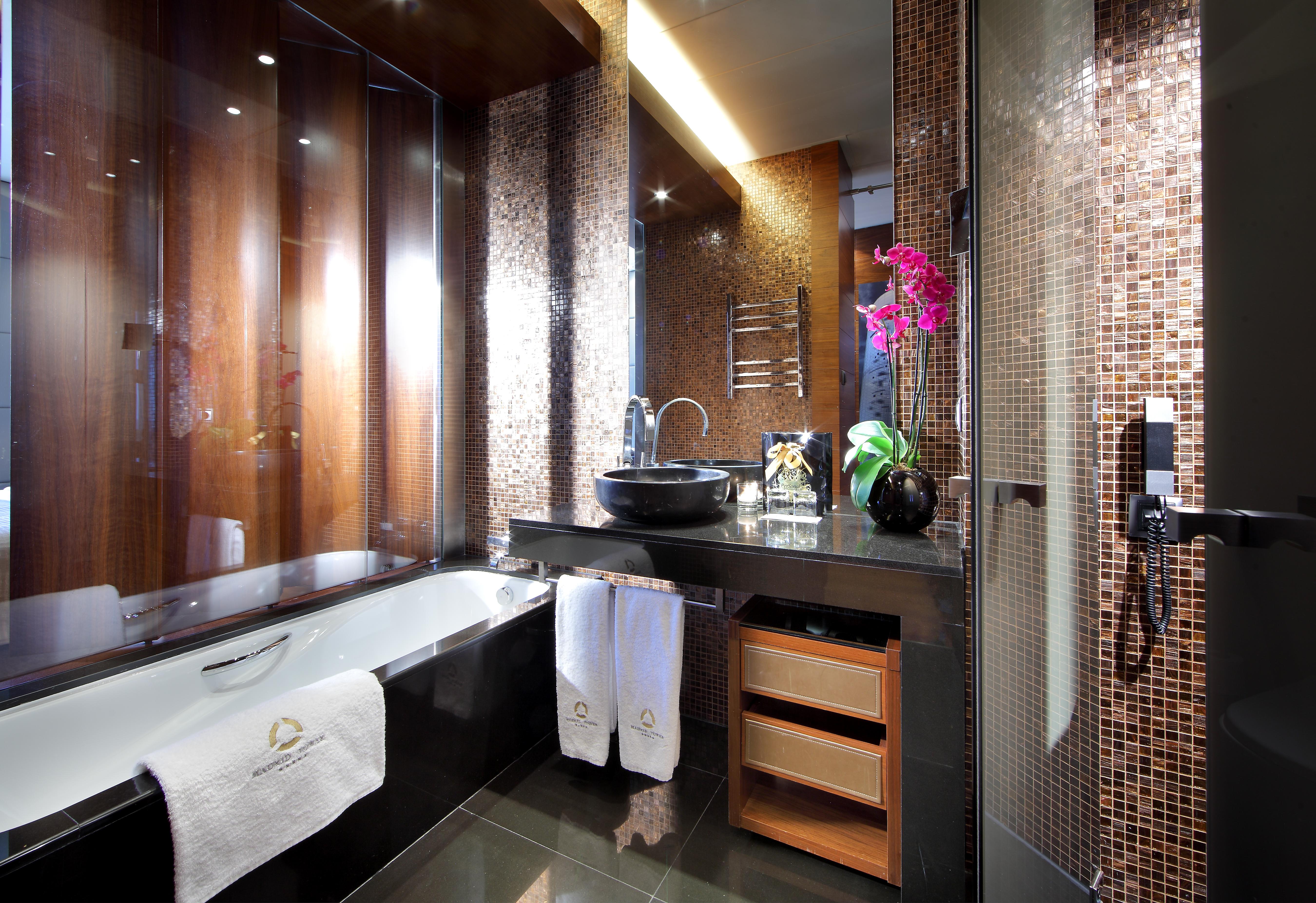 Hotel Eurostars Madrid Tower Esterno foto The photo shows a modern and elegantly designed bathroom. It features a luxurious bathtub on the left, accompanied by fluffy white towels. The sink area has a sleek black countertop with an artistic bowl sink, and there are various decorative element