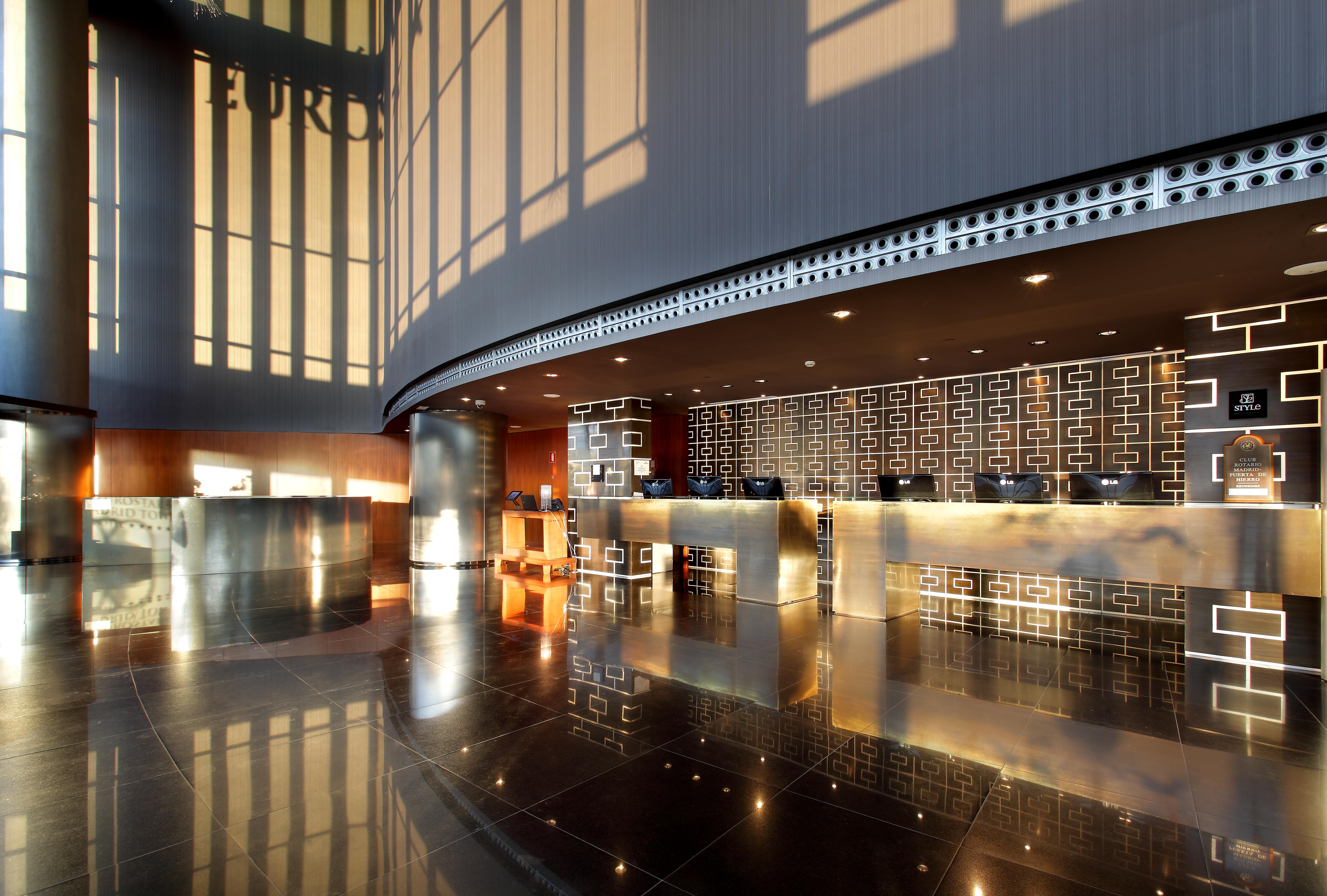 Hotel Eurostars Madrid Tower Esterno foto The photo shows the interior of a modern hotel lobby. It features a sleek reception desk with a polished surface and an elegant design. The lobby has large windows allowing natural light to flood in, creating a bright and inviting atmosphere. The flo