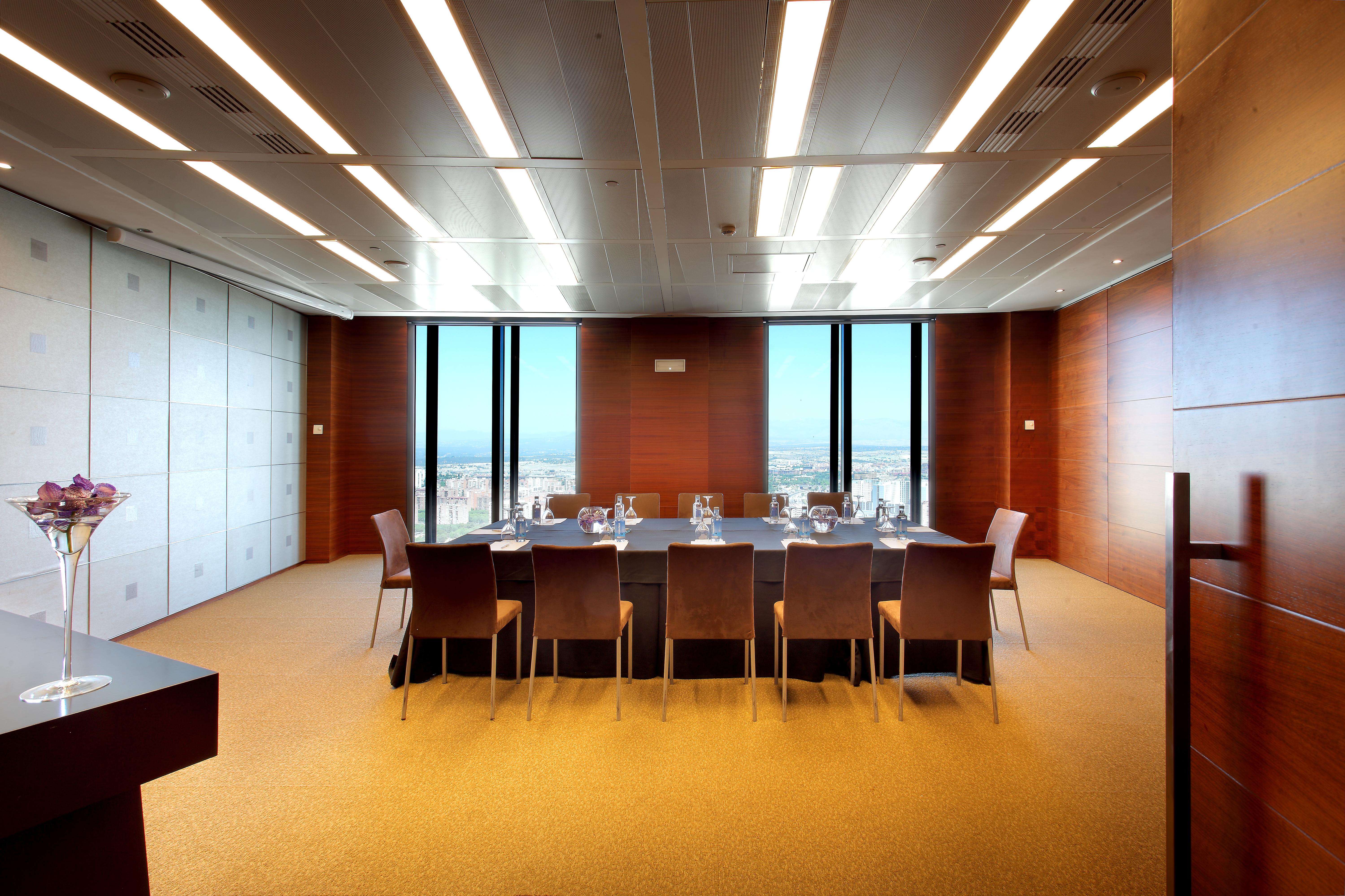 Hotel Eurostars Madrid Tower Esterno foto The photo shows a modern conference room or meeting space. It features a large rectangular table surrounded by several leather chairs. The room has wooden paneling and large windows that let in natural light, providing a view of the outside landscape