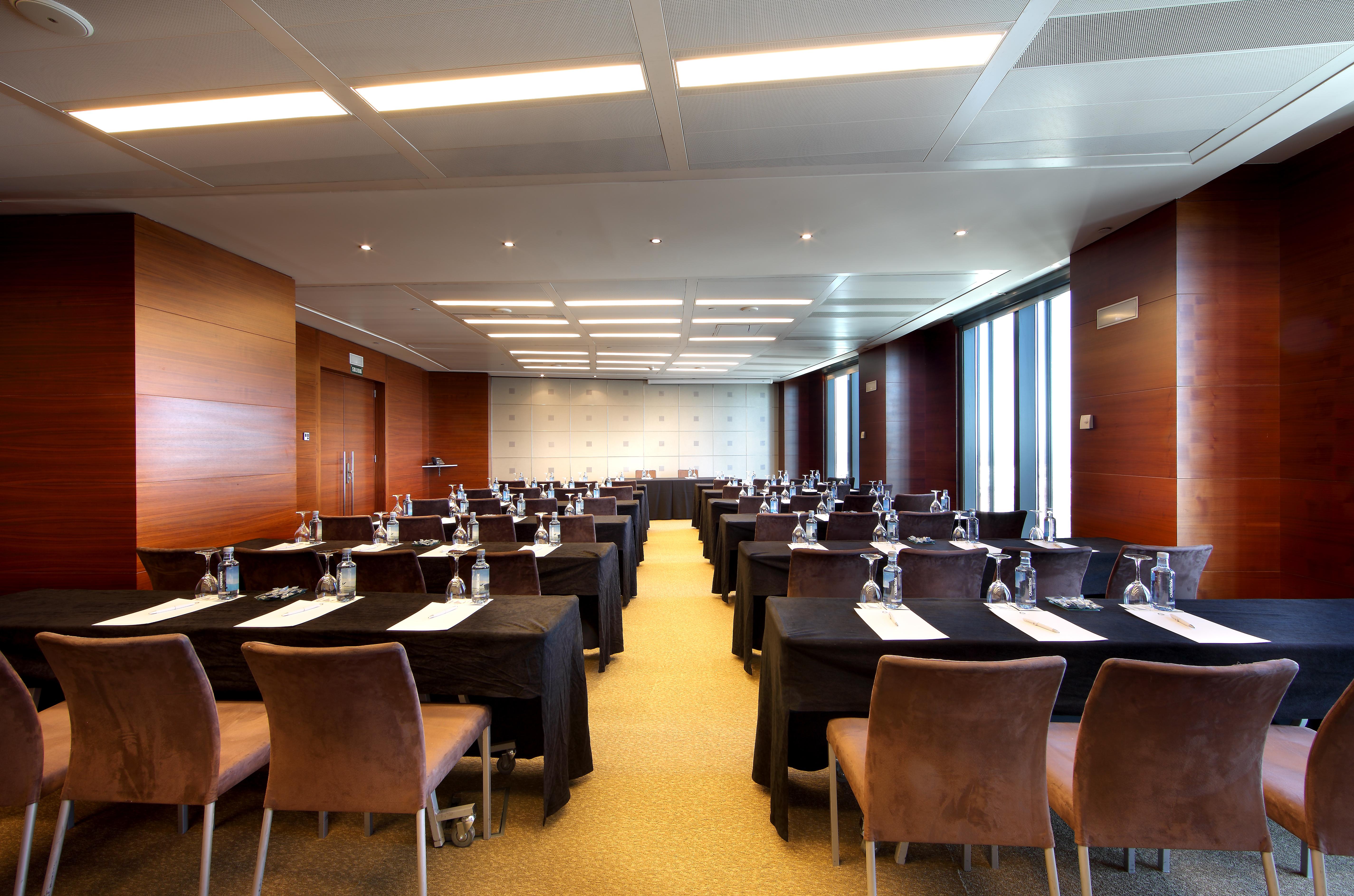 Hotel Eurostars Madrid Tower Esterno foto The photo shows a modern conference room set up for a meeting or seminar. There are multiple tables arranged in rows, each covered with black tablecloths. Each table has a clean white sheet, and water bottles are placed at each setting. The room is w