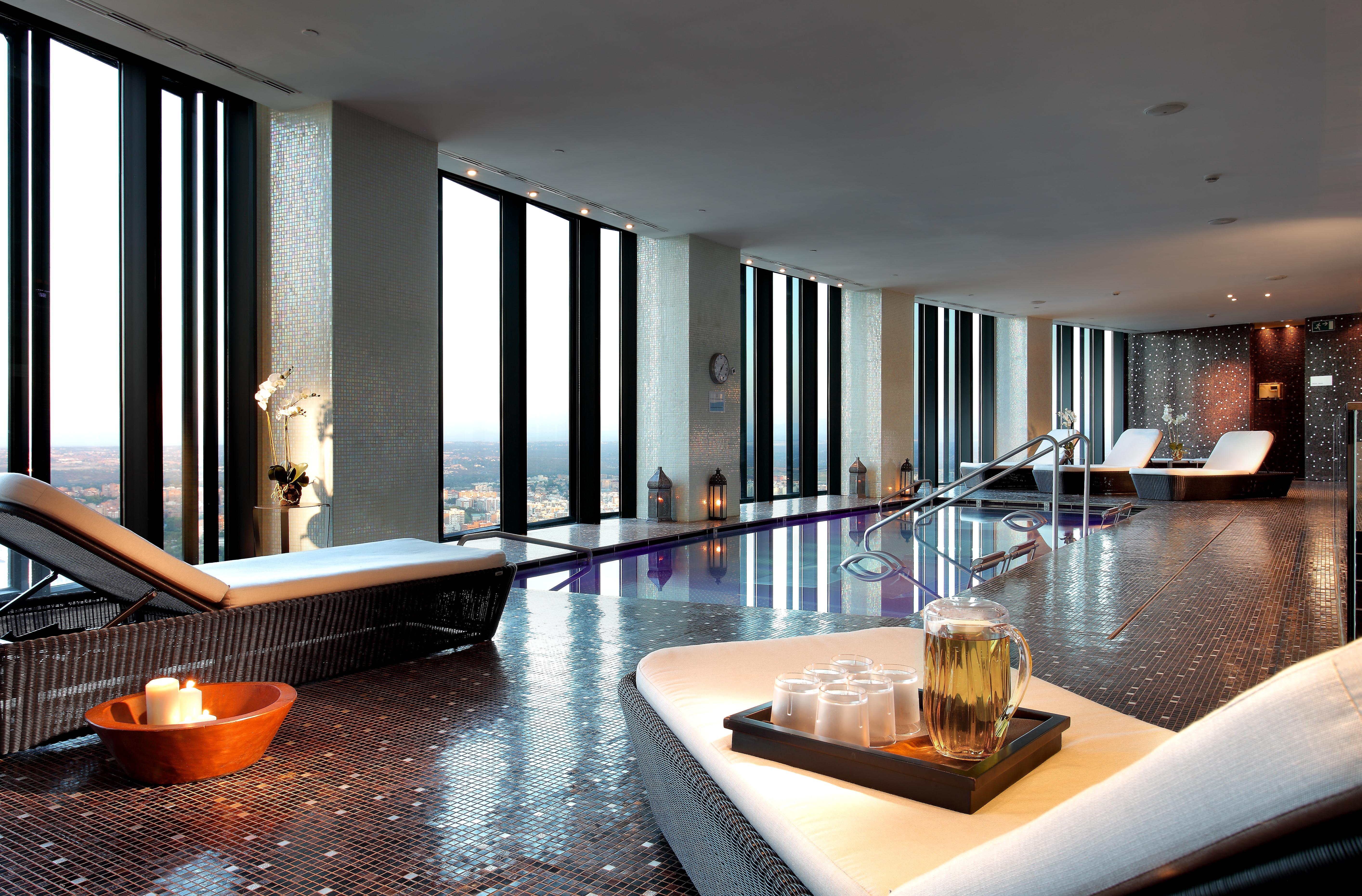 Hotel Eurostars Madrid Tower Esterno foto The photo depicts a luxurious spa interior with large windows that offer a panoramic view of the outside. The space features sleek, modern lounge chairs and a tranquil atmosphere. There is a pool area, and the floor is tiled with reflective materials