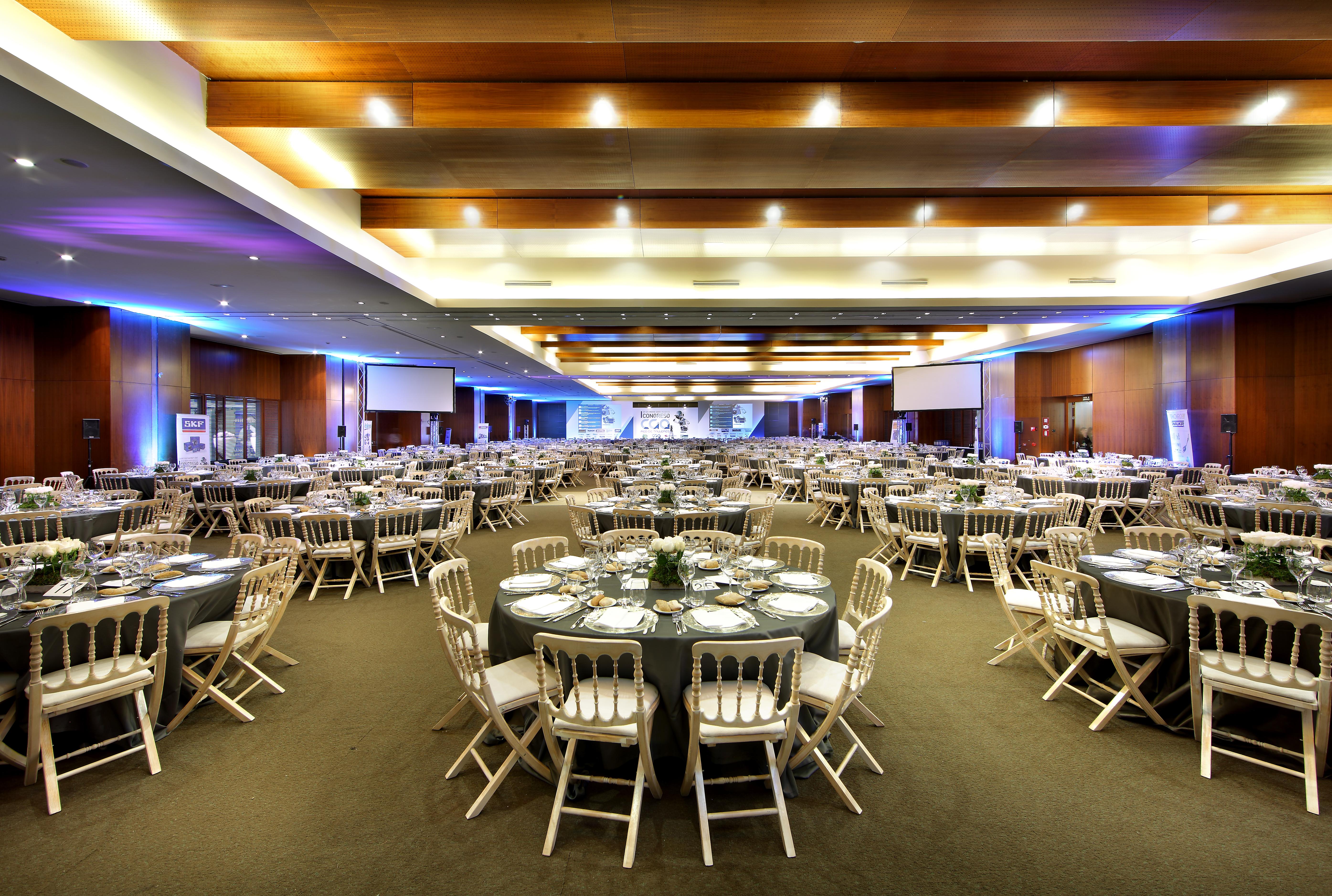 Hotel Eurostars Madrid Tower Esterno foto The photo shows a large banquet hall set up for an event. The room is filled with numerous round tables, each adorned with dark tablecloths and decorative centerpieces. There are white chairs arranged around the tables. The lighting is soft, with a c