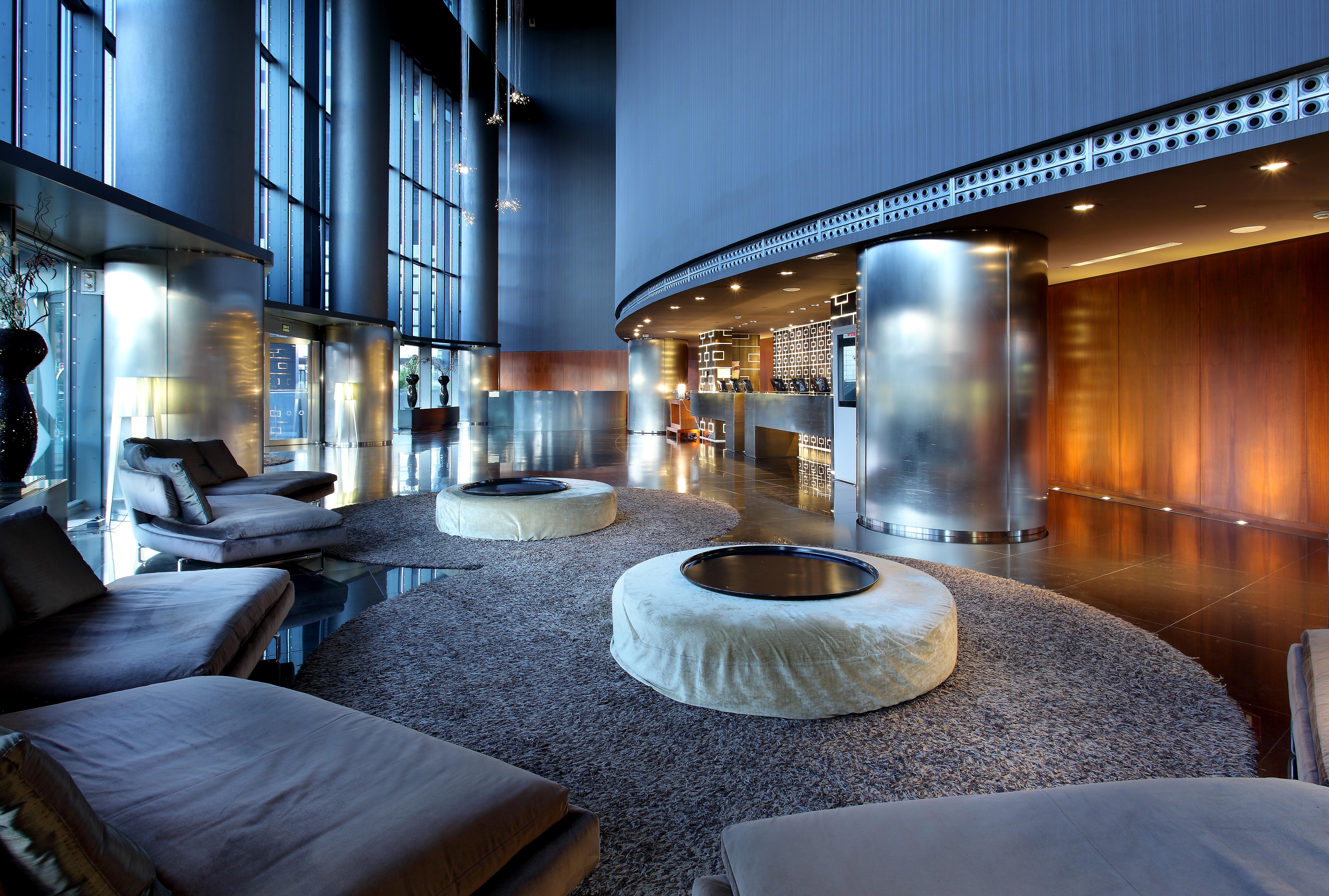 Hotel Eurostars Madrid Tower Esterno foto The photo depicts a modern and stylish lounge area. The space features light-filled windows that allow for ample natural light, creating an airy atmosphere. There are several circular seating arrangements with plush, low-slung cushions arranged aroun