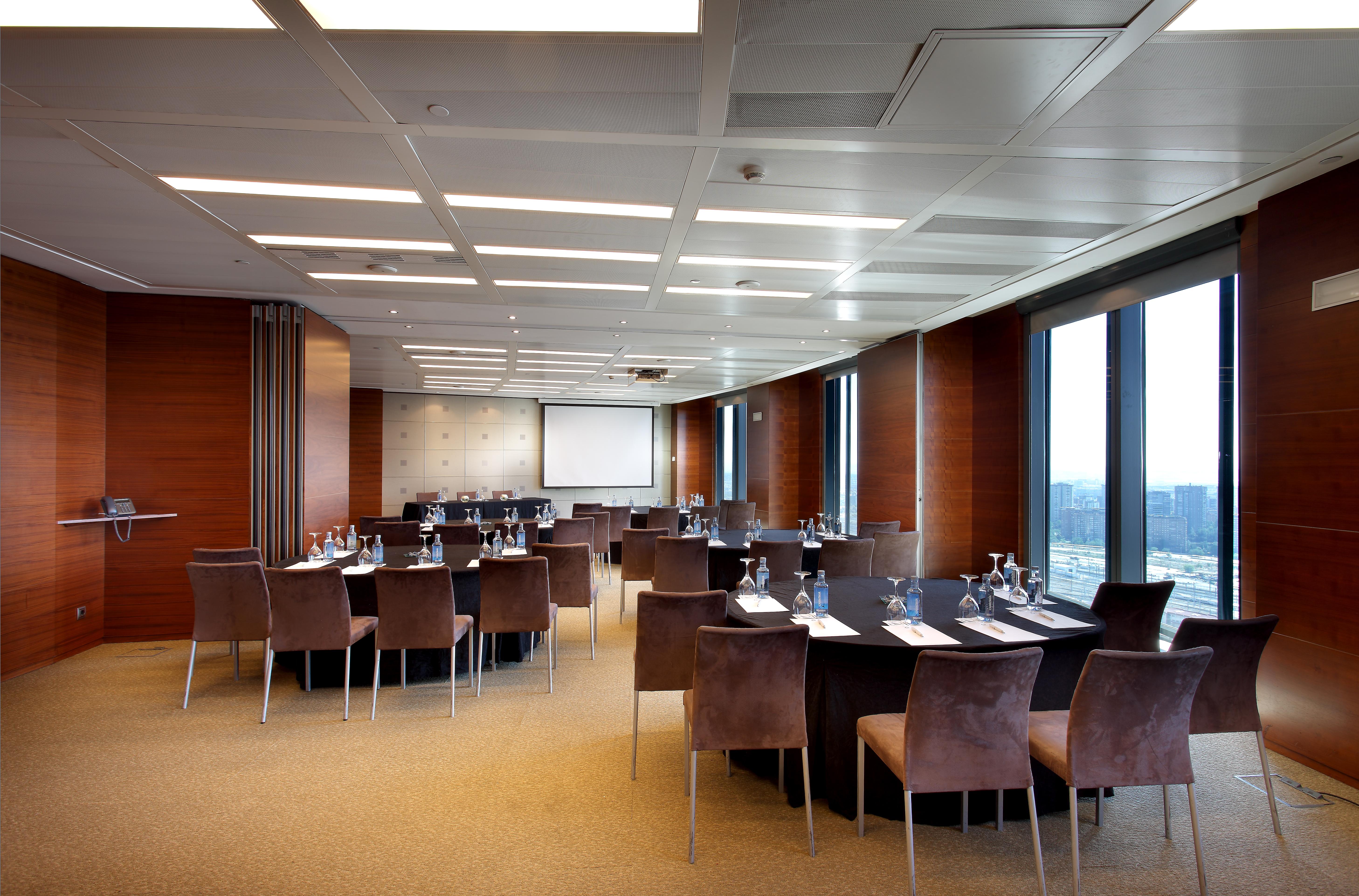 Hotel Eurostars Madrid Tower Esterno foto The photo shows a modern conference room set up for a meeting or event. The room features a large, rectangular table surrounded by upholstered chairs. Each place at the table has a notepad and pen, and there are glasses of water provided. Large windo