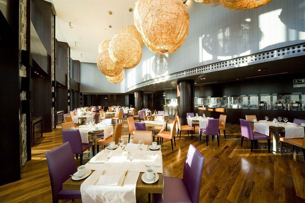 Hotel Eurostars Madrid Tower Ristorante foto The photo shows a modern restaurant interior featuring elegant decor. The dining area includes tables set for guests with white tablecloths, plates, and cutlery. The seating consists of a mix of wooden chairs, some upholstered in purple fabric. The l