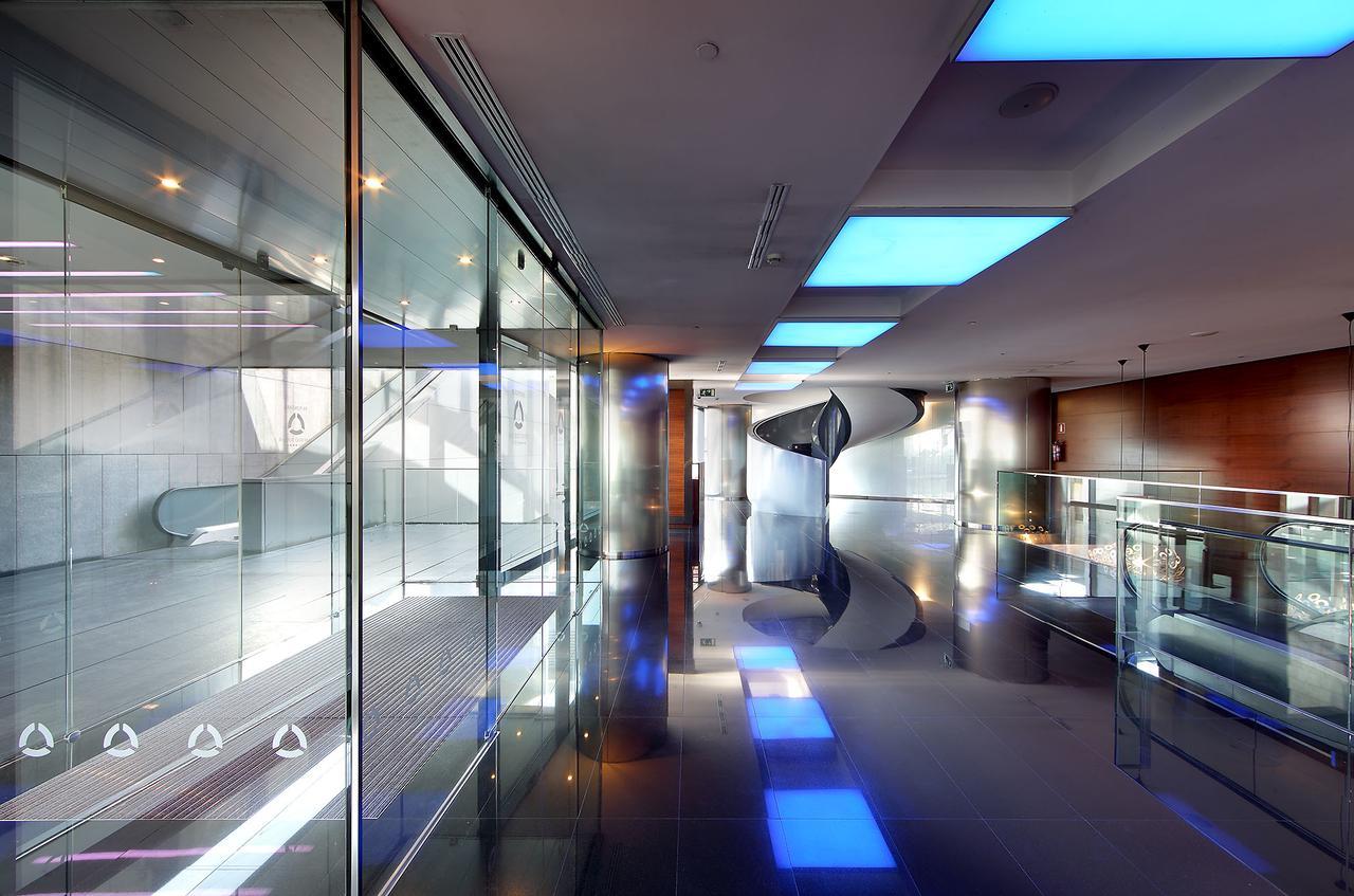 Hotel Eurostars Madrid Tower Esterno foto The photo shows a modern, sleek interior space characterized by large glass walls and reflective surfaces. The ceiling features blue-lit sections, creating a contemporary atmosphere. The polished floor enhances the overall brightness of the area, and