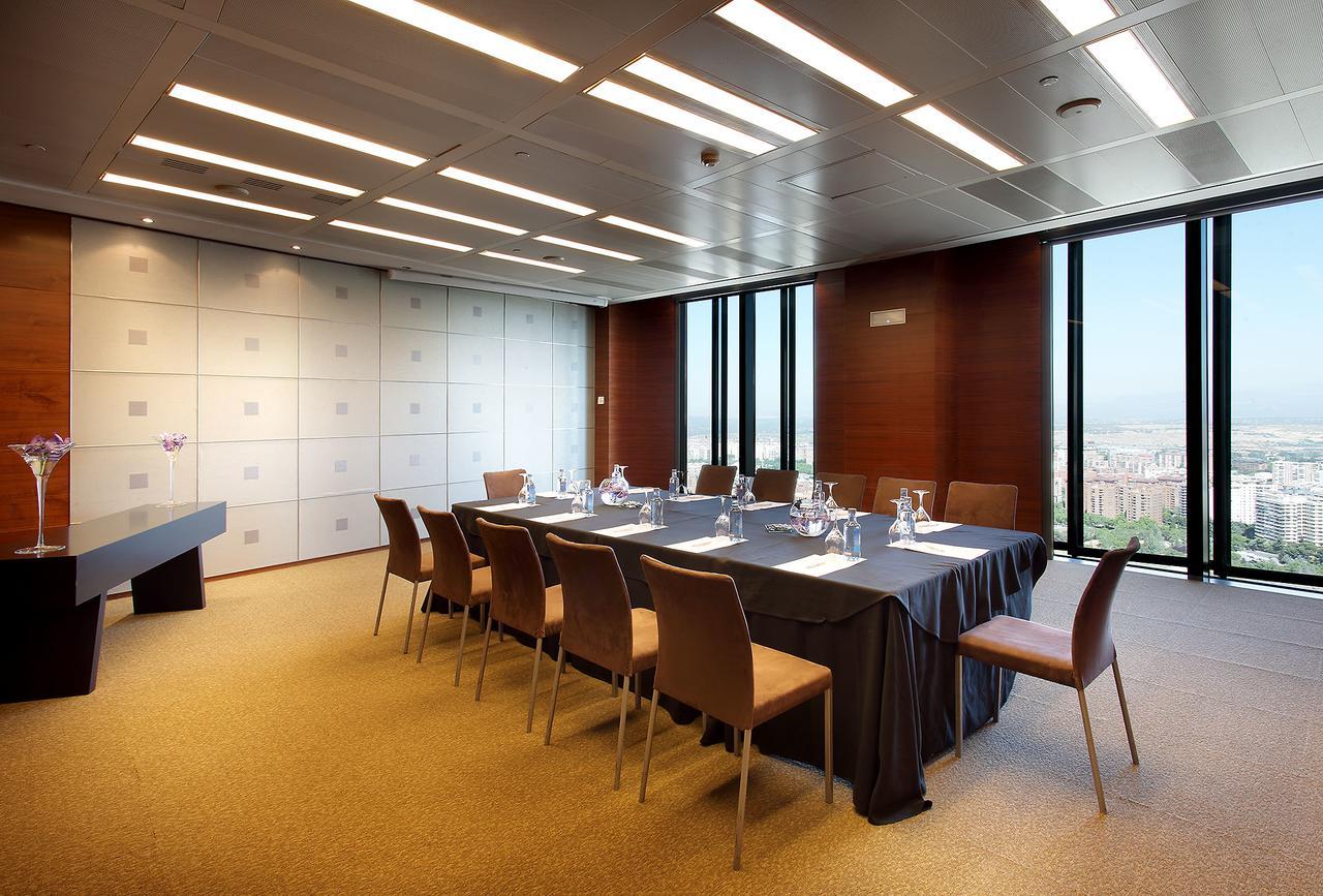 Hotel Eurostars Madrid Tower Esterno foto The photo shows a modern conference room with a long table set up for meetings. There are several chairs around the table, and the table is covered with a dark tablecloth. On the table, there are glass pitchers and cups, indicating it is prepared for