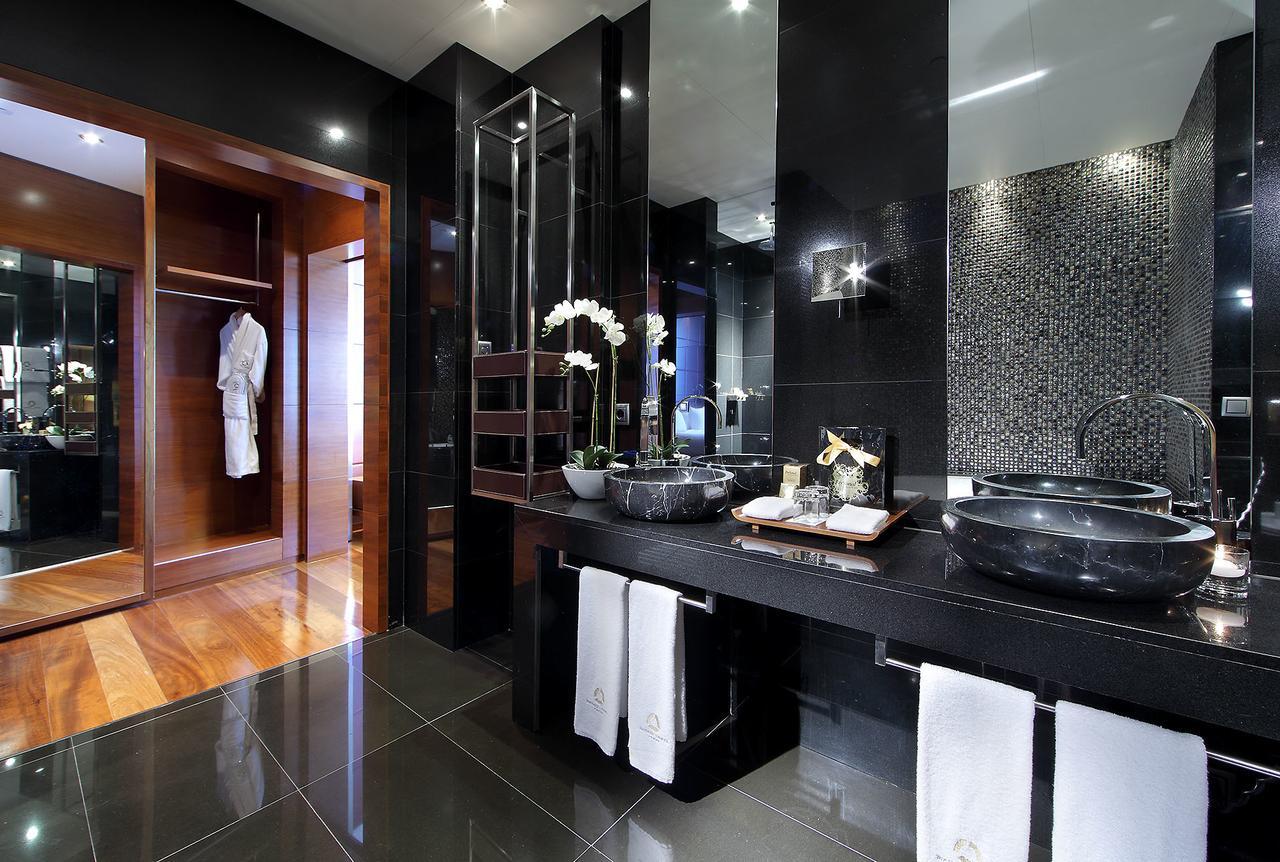 Hotel Eurostars Madrid Tower Esterno foto The photo shows a modern and elegant bathroom with a contemporary design. It features dual black stone sinks with sleek faucets positioned on a dark countertop. The walls are adorned with shiny black tiles and a mosaic pattern, contributing to a luxu