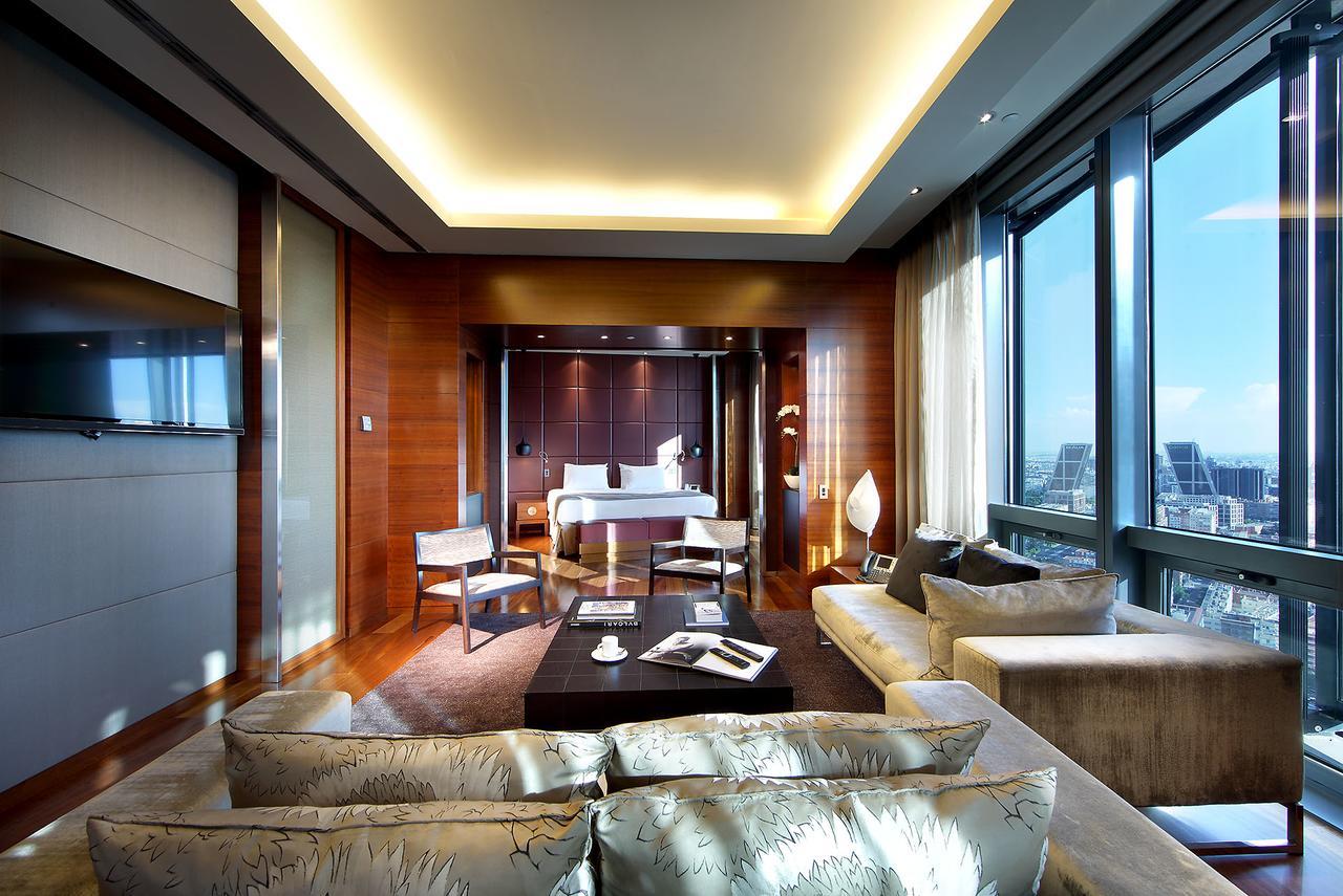 Hotel Eurostars Madrid Tower Esterno foto The photo shows a luxurious hotel room or suite with a modern design. It features large windows that offer a view of the outside, letting in plenty of natural light. The interior has warm wooden accents on the walls and sophisticated lighting through