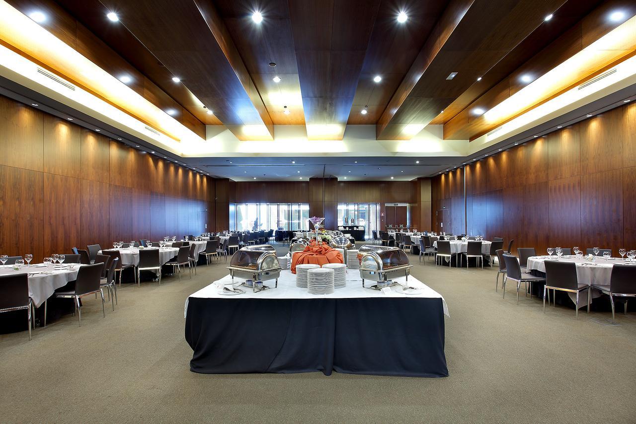 Hotel Eurostars Madrid Tower Esterno foto The photo shows a spacious banquet hall or dining area with a modern design. The room features wooden walls and a high ceiling with lighting that creates a warm ambiance. In the center, there is a large table draped in black cloth, adorned with food 