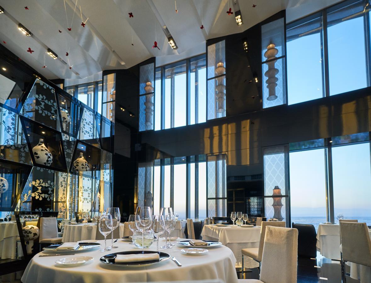 Hotel Eurostars Madrid Tower Esterno foto The photo shows an elegant restaurant interior featuring a modern design. The space has large windows that provide a view of the outside, allowing natural light to fill the room. The decor includes artistic elements, such as sculptures and decorative