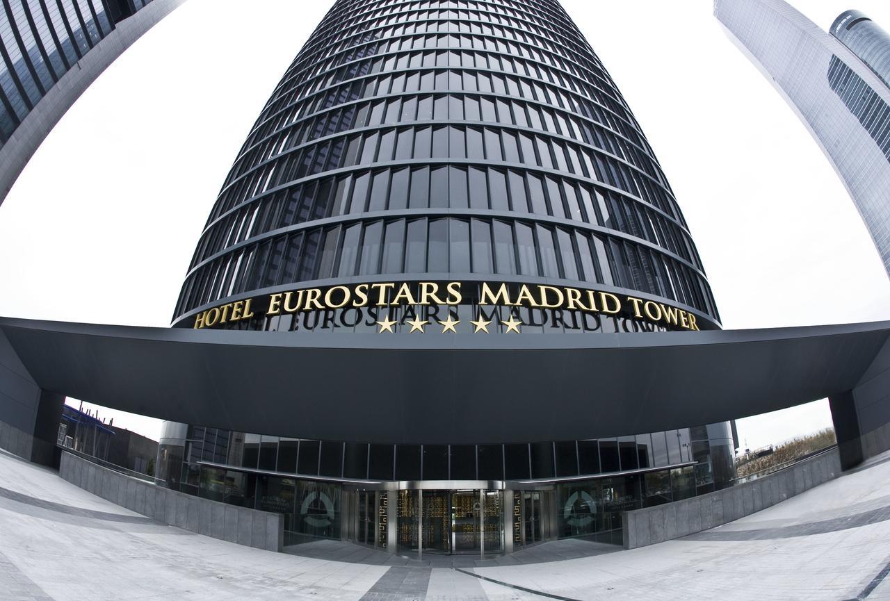 Hotel Eurostars Madrid Tower Esterno foto The photo shows a tall, modern glass building that serves as the Eurostars Madrid Tower Hotel. The building features a sleek, curved design with a prominent entrance. Above the entrance, the hotel's name is displayed in large golden letters, indicati