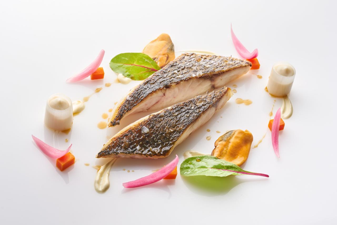 Hotel Eurostars Madrid Tower Esterno foto The image depicts a beautifully plated dish featuring two pieces of fish fillet, likely a type of white fish, arranged artfully on a white plate. The fish has a crispy skin and is cooked to a tender texture. Surrounding the fish are various garnishes