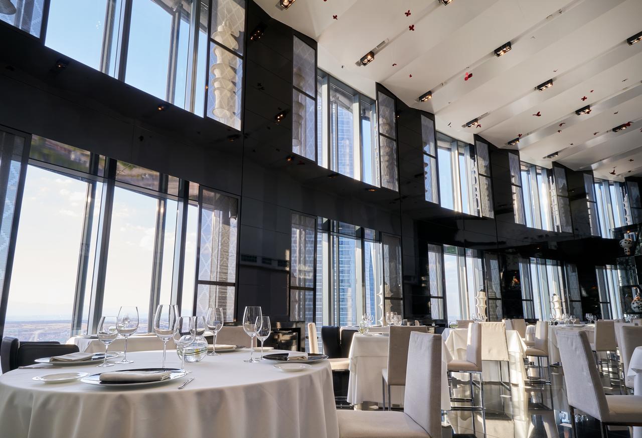 Hotel Eurostars Madrid Tower Esterno foto The photo depicts an elegant restaurant interior characterized by sleek, modern design. It features large floor-to-ceiling windows that allow abundant natural light to fill the space and provide a panoramic view of the outside. The dining area includ