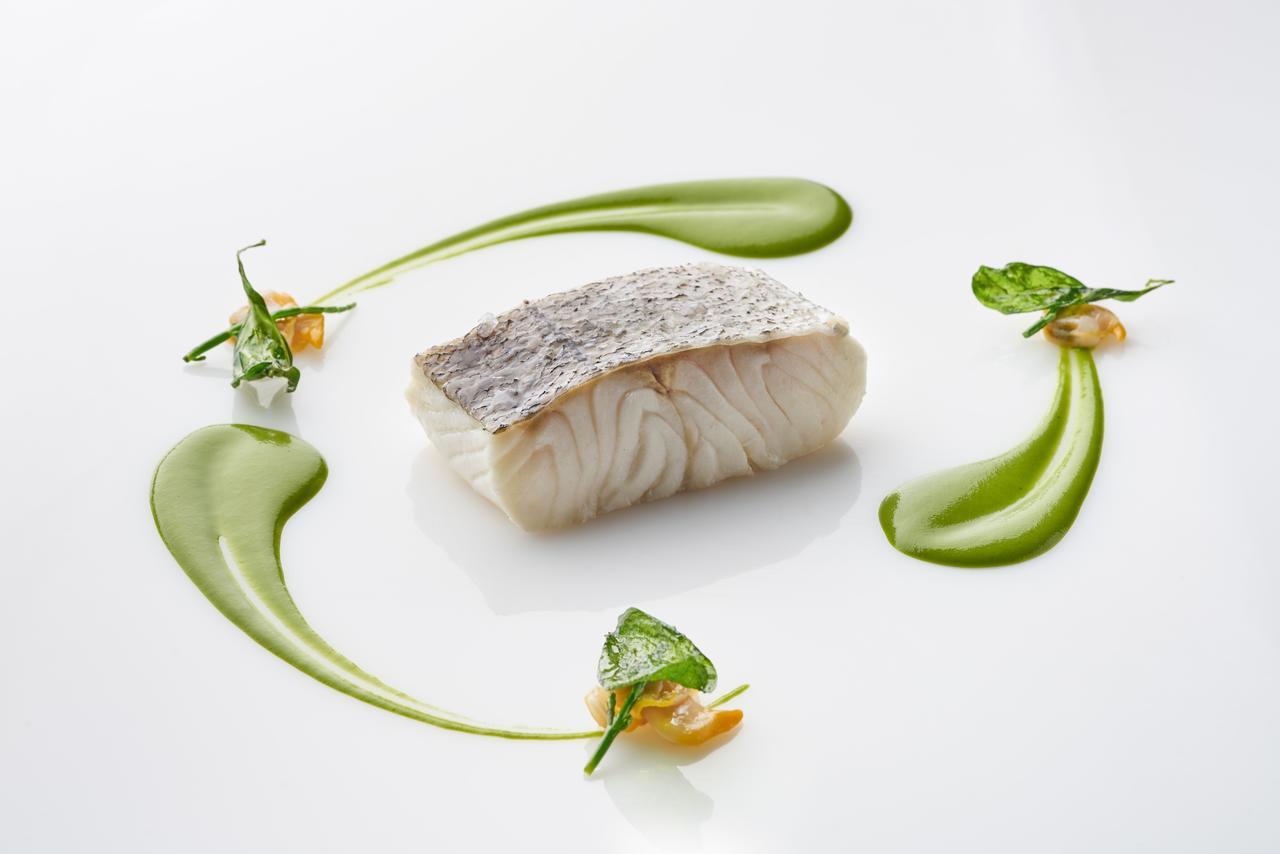 Hotel Eurostars Madrid Tower Esterno foto The photo shows a beautifully presented dish featuring a piece of fish, likely a white fish, with a prominent skin side on top. It is surrounded by artistic garnishes, including vibrant green sauces and small sprigs of herbs. The composition is elega