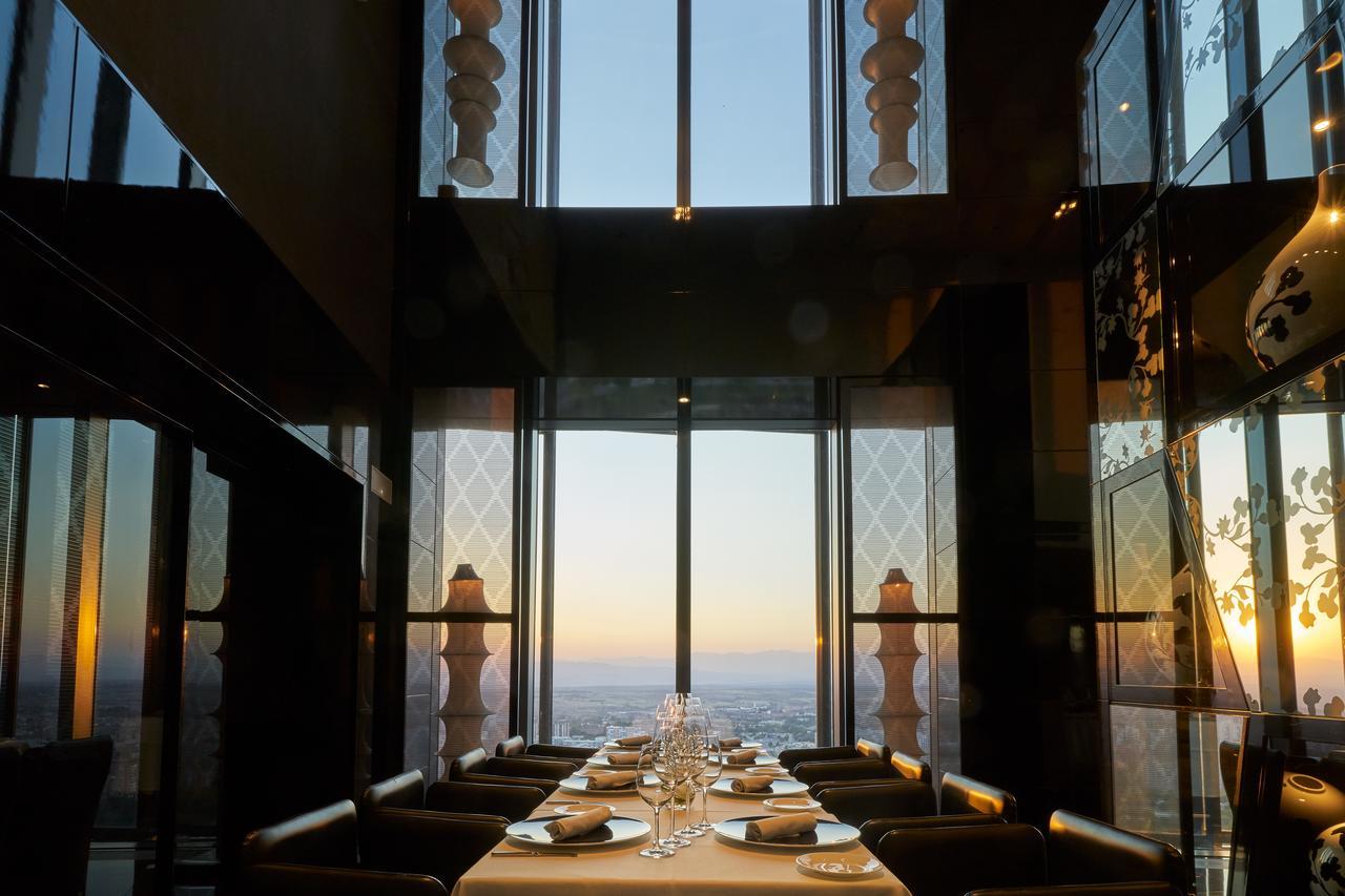 Hotel Eurostars Madrid Tower Esterno foto The photo shows an elegantly set dining table in a restaurant with large glass windows. The view from the windows reveals a sunset, casting warm colors over the landscape. The table is tastefully arranged with plates and glassware, suggesting a fine 