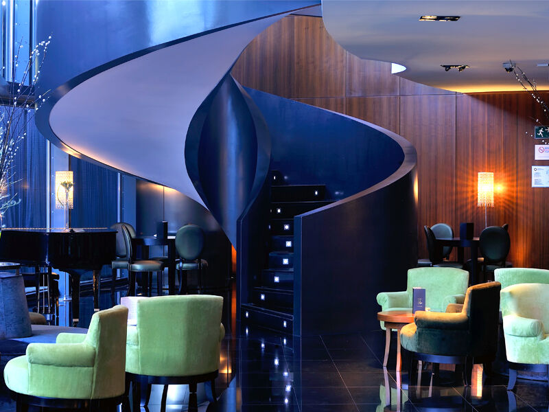 Hotel Eurostars Madrid Tower Esterno foto The photo depicts a stylish and modern interior, likely of a bar or lounge. The focal point is a unique spiral staircase that has a sleek, flowing design, leading to another level. The surrounding area features a combination of dark wood panels and g