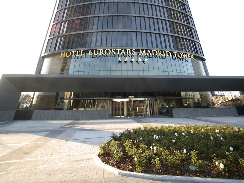 Hotel Eurostars Madrid Tower Esterno foto The photo shows the exterior of the Eurostars Madrid Tower Hotel, which is a modern, high-rise building. The hotel features a sleek glass facade and has "HOTEL EUROSTARS MADRID TOWER" prominently displayed in gold lettering above the entrance. The ar